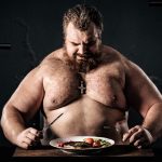 Shirtless muscular man eating a nutritious meal, symbolizing strength and health.